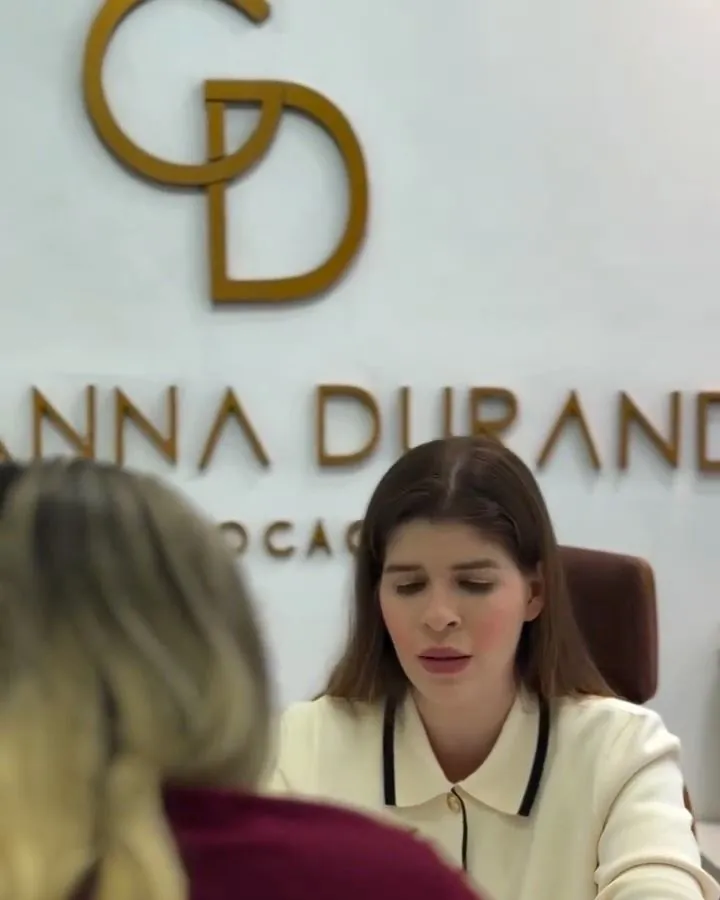 Giovanna atendendo uma cliente na mesa, diante da parede com o logo dourado