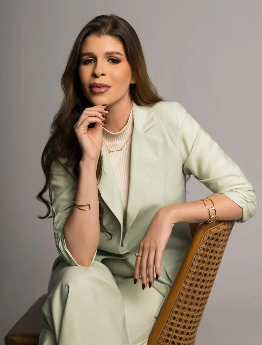 Giovanna Durando sentada numa cadeira de palhinha, de conjunto verde-sálvia, com a mão no queixo