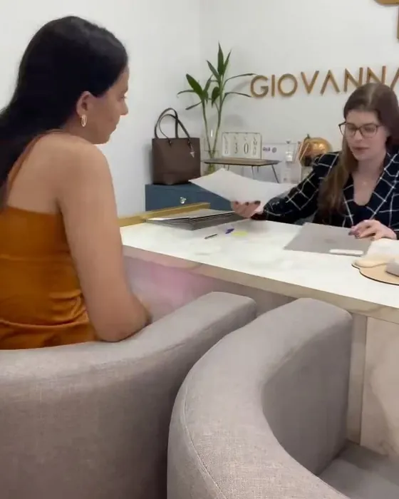 Recepção do escritório com poltronas claras e uma cliente sendo atendida